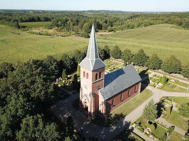 Rød murstenskirke med gråt tag og tårn som er Brande kirke
